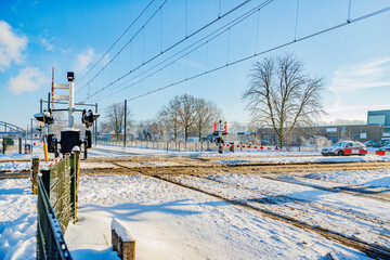 Snow covered railway crossing on road in winter landscape, closed downward barriers, stop sign and...