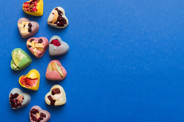 chocolate sweets in the form of a heart with fruits and nuts on a colored background. top view with space for text, holiday concept