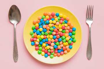 cutlery on table and sweet plate of candy. Health and obesity concept, top view on colored background