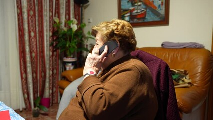Elderly woman sitting talking on the phone, on her arm she wears a SOS bracelet