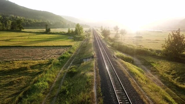 Fly over railway in green landscape of rice paddy farm fields in forest mountain foothills wonderful scenic wide view of nature in rural countryside local people traditional culture life in Iran Gilan