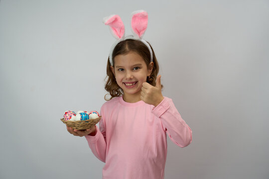 Girl wearing pink bunny ears and shirt and holding basket with colorful Easter eggs