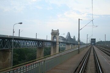 A long railway track stretches into the distance, with a majestic bridge towering in the background.