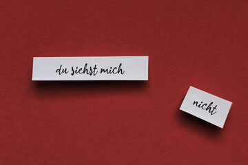 Weiße Zettel mit  du siehst mich nicht flach auf einem farbigen Untergrund, aus der Draufsicht...