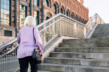 rear view of unrecognizable senior woman walking up stairs, concept of elderly people leisure and...