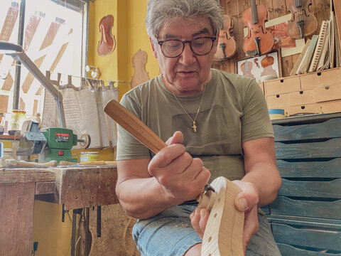 master luthier violin maker working on violin scroll in his workshop - Powered by Adobe