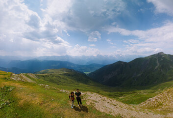 Couple woman and man wearing wide sun hat and backpack, tourists on hiking trail to Koruldi Lakes, Svaneti region, Mestia Georgia. travel and active recreation. Summer day. Aerial large panorama