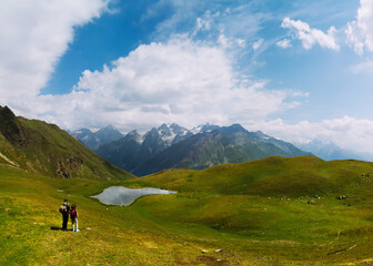 Fototapeta na wymiar Aerial view at the Koruldi lakes. Couple of hikers. Green hills, high mountain pastures. Summer day. in the background are the snowy peaks of the Caucasus Mountains. The concept of active recreation.