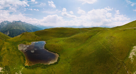 Aerial view at the Koruldi lakes. Green hills, high mountain pastures. Summer day. in the background are the snowy peaks of the Caucasus Mountains. High resolution panorama - obrazy, fototapety, plakaty
