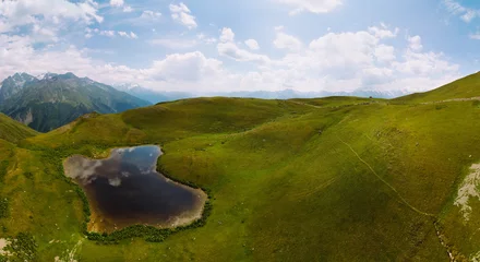 Fotobehang Aerial view at the Koruldi lakes. Green hills, high mountain pastures. Summer day. in the background are the snowy peaks of the Caucasus Mountains. High resolution panorama © Sergey