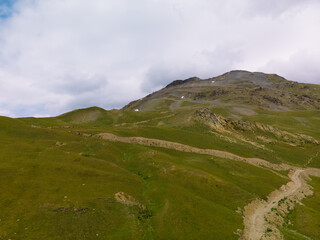 Fototapeta premium Aerial view at the Koruldi lakes. Green hills, high mountain pastures. Summer day. in the background are the snowy peaks of the Caucasus Mountains. road, trail to Ushba