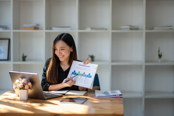 Naklejka premium Smiling businesswoman looking at laptop screen and showing data clipboard holding in her hand. Video conference