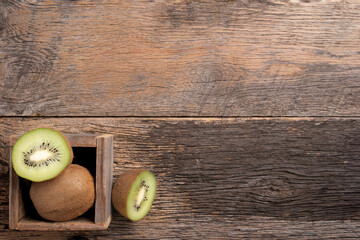 Kiwi fruit sliced in half and whole in a wooden box on a wooden background.