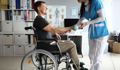 Doctor helps man on wheelchair hold dumbbell. Strengthening human parts, ability to part with...