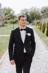 Portrait of the groom in nature in the summer. Stylish tall groom in an elegant black business suit. Businessman in nature. Portrait of a successful man. Wedding portrait of the groom.