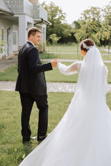 A handsome groom and an elegant bride in a lush white dress are walking in a summer park. Happy bride and groom getting ready for their best day.