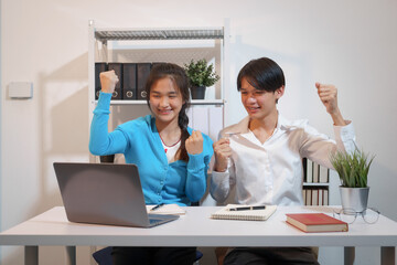 An Asian male consultant and an African American female intern sit at a table with laptops doing...
