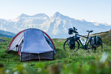 Setting up camp during bike travel in the Alps with tent and a packed bike in the foreground and a high mountain range in the background