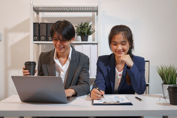 An Asian male consultant and an African American female intern sit at a table with laptops doing paperwork together to discuss a project's financial reports. Company business collaboration concept