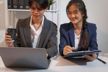 Obraz premium An Asian male consultant and an African American female intern sit at a table with laptops doing paperwork together to discuss a project's financial reports. Company business collaboration concept