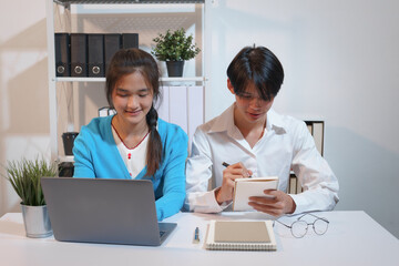 Obraz premium An Asian male consultant and an African American female intern sit at a table with laptops doing paperwork together to discuss a project's financial reports. Company business collaboration concept