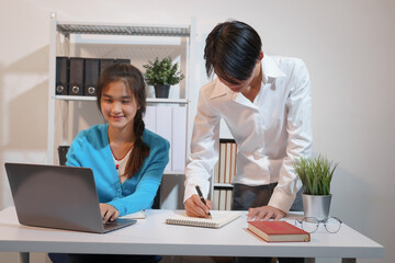 An Asian male consultant and an African American female intern sit at a table with laptops doing paperwork together to discuss a project's financial reports. Company business collaboration concept