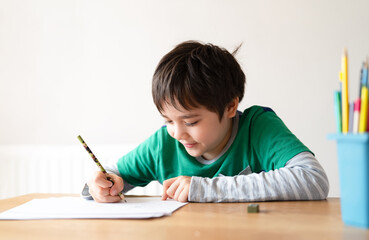 Education concept,School kid using black colour pen drawing or sketching on paper,Portrait boy siting on table doing homework in living room,Child enjoy art and craft activity at home