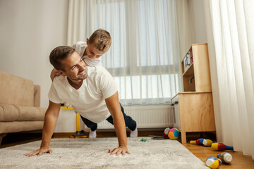 A father is doing pushups while is son is on his backs.
