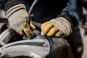 Close up of hands holding a hose and pumping a car tire at vulcanizing workshop.