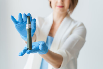 A female cosmetologist in gloves holds a dermopen for mesotherapy in her hands. Cosmetic procedures, beauty salon, facial skin care