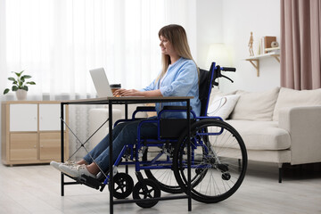 Woman in wheelchair using laptop at table in home office