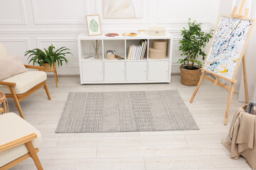 Stylish room with beautiful rug, easel and furniture. Interior design