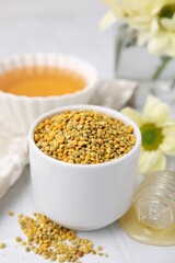 Fresh bee pollen granules and dipper with honey on white table, closeup