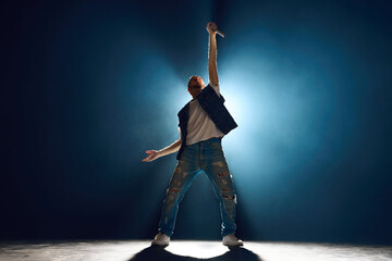 Street style singer gesturing with hand on stage against dark background. Spotlight and smoke creating silhouette effect. Concept f music and dance, lifestyle, festivals, concerts, self-expression.