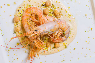 Gamberi freschi cotti sulla piastra e serviti su una crema di ceci con ceci interi e granella di pistacchio come secondo piatto in un ristorante elegante