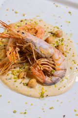 Gamberi freschi cotti sulla piastra e serviti su una crema di ceci con ceci interi e granella di pistacchio come secondo piatto in un ristorante elegante