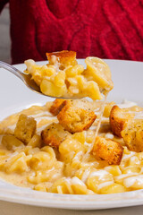 Piatto di pasta e patate con provola filante, crema di formaggio e crostini di pane croccanti servito come primo piatto in un ristorante elegante