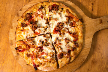 Pizza rotonda cotta nel ruoto condita con mozzarella, peperoni e salsiccia poggiata su un tagliere...