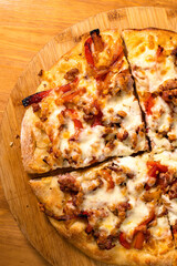 Pizza rotonda cotta nel ruoto condita con mozzarella, peperoni e salsiccia poggiata su un tagliere di legno di una rosticceria