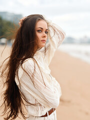 Fototapeta premium Serene Summer Beauty: A Young Attractive Woman Posing Outdoors on a White Sandy Beach by the Calm Ocean, Her Brunette Hair Flowing in the Wind, Wearing a Stylish Bikini under the Sunny Blue Sky