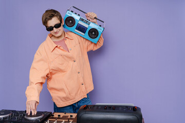 Photo of young DJ hold boom box  and playing music on a turntable  on color background