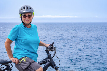 Happy active senior cyclist woman enjoying riding with her bicycle at sea. Elderly lady with helmet...