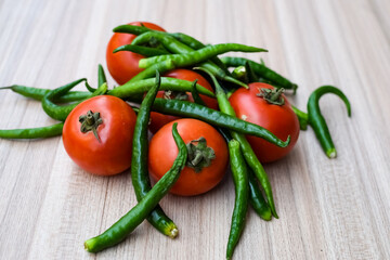 Red tomato and green chili pepper on plain wooden table, green essential vegetables for all essential foods, view of unpeeled vegetables with plain background