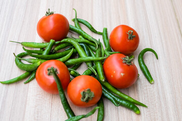 Red tomato and green chili pepper on plain wooden table, green essential vegetables for all essential foods, view of unpeeled vegetables with plain background