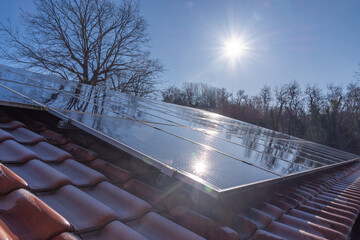 Solarmodule auf einem Hausdach reflektieren die Winter Sonne vor einem klaren blauen Himmel,...