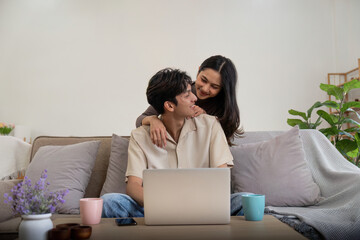 Fototapeta premium Young couple asian using laptop together while sitting on sofa at home