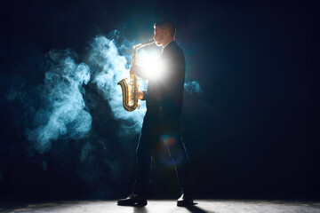 Musician with saxophone performing piece on stage with smoke. Backlit creating silhouette effect....