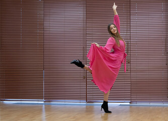 Pretty girl, attractive ballerina in pink dress, dances in modern interior.