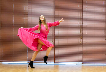 Pretty girl, attractive ballerina in pink dress, dances in modern interior.