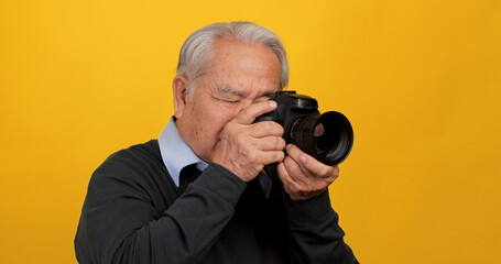 Old Asian man taking photo with digital camera, isolated on yellow background in the studio.